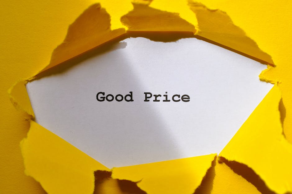 A close-up of a white card with the words 'Good Price' printed in black, partially visible through a torn yellow paper background. The torn edges of the yellow paper are irregular, revealing the white