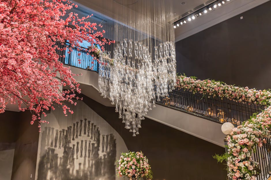 A luxurious interior featuring a floral arrangement with pink and white roses, peonies, and greenery adorning a black wrought iron staircase railing, complemented by a large pink cherry blossom tree o