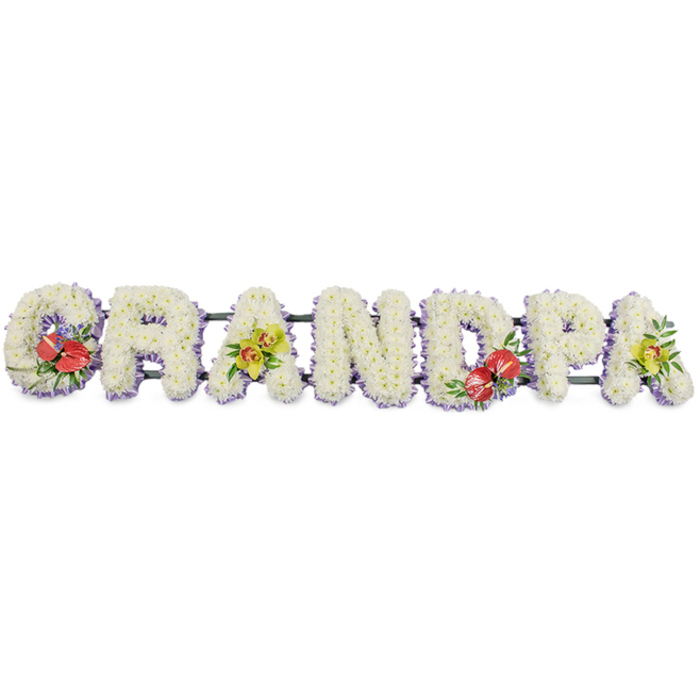 This image shows a dignified floral name tribute spelling "GRANDPA" in robust capital letters, arranged in a single horizontal line as it would appear on a stand at a funeral service in Harringay or at a local chapel near Finsbury Park. Each letter is built from a solid base and then completely covered with hundreds of small white chrysanthemums, placed closely together so that no gaps of foliage show through. The effect is a soft, quilted surface of pure white, with each bloom catching the light differently, giving depth and gentle movement across the word. A band of pale lavender ribbon curves neatly along the lower edge of each letter, almost like a shadow of colour, outlining the crisp shapes and introducing a hint of calm pastel tone. Behind the flowers, dark green support bars connect the letters, providing structure while remaining largely hidden from view. Carefully positioned floral sprays add character and heartfelt colour. On the left, the "G" is decorated with a vivid grouping of deep red anthuriums, their high-gloss, heart-shaped petals and yellow spadices framed by dark, leafy greens. Moving along, the first "A" features yellow-green orchids, their slender stems and open faces giving a lighter, more airy touch. The "D" repeats the bold anthurium detail, and the final "A" is crowned with another spray of yellow-green orchids and greenery, visually balancing the piece. Created in the calm, respectful style local families often request from Harringay florists, this tribute feels like a loving final message to a grandfather, full of quiet gratitude and remembrance.